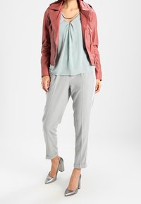 Röd skinnjacka, ljusblå blus med en veck, grå avsmalnande byxor och metallic silver klackskor. Mjuka texturer och modern design.