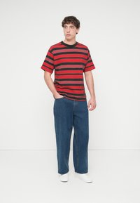 Κόκκινη και μαύρη ριγέ κοντομάνικη μπλούζα, σε συνδυασμό με μπλε τζιν παντελόνι με ίσια γραμμή και λευκά αθλητικά παπούτσια. Απλός, καθημερινός σχεδιασμός ρούχου.