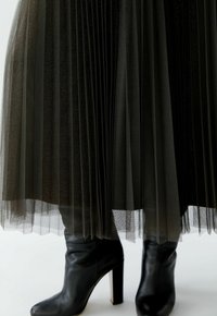 Black pleated skirt made of sheer fabric with a slight shimmer, paired with black ankle boots featuring a high heel and smooth texture.