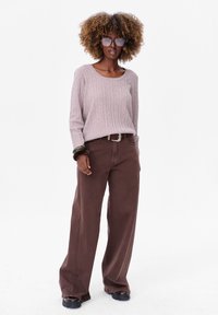 Lichtroze ribgebreide trui met een ronde halslijn, gecombineerd met bruine wijde broek. Gestyled met een zilveren riem en chunky zwarte schoenen.