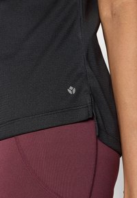 Fekete, texturált sportpóló apró szürke logóval az alján, bordó leggingsszel, amely íves varrást díszít.