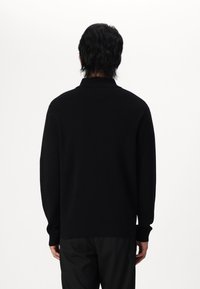 Svart strikket genser med polo-krage, lange ermer og en avslappet passform. Myk tekstur, minimalistisk design, ingen synlig merkevare eller mønstre.