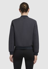 Tumesinine pommitaja jakk, millel on sile tekstuur, soonikkoes varrukad ja alläär ning minimalistlik disain. Ei ole nähtavaid logosid ega kaunistusi.