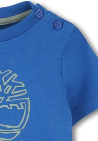 Korte mouwen blauwe T-shirt van zachte katoen, met een groene grafische print en twee drukknoopjes op de schouder voor eenvoudig aan- en uittrekken.