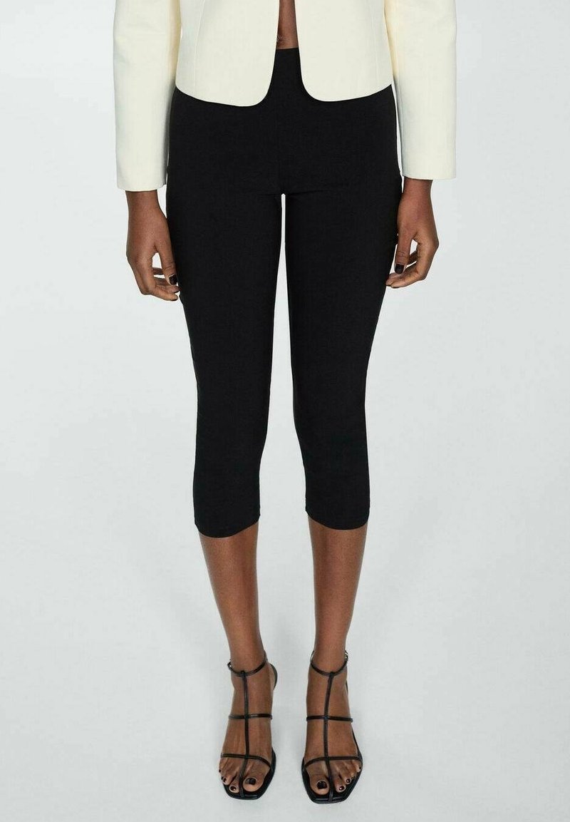 Leggings capri noirs en tissu extensible, associés à des talons hauts noirs à lanières. Le haut est un blazer blanc ajusté.