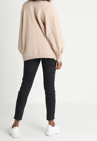 Beige oversized svetr s balónovými rukávy, zkombinovaný s černými skinny džínami a bílými teniskami. Měkká textura a volný střih.