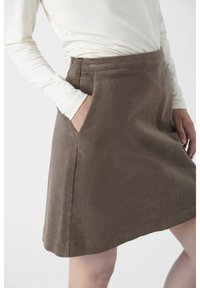 Bruine corduroy rok met zijzakken, met een rechte snit en een zachte textuur. Gekozen met een crèmekleurige top met lange mouwen tegen een neutrale achtergrond.