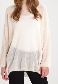 Pull léger de couleur crème avec une coupe ample, des manches longues et un effet ombré gris progressif en bas. Tricot doux et texturé.