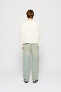 Tenue décontractée comprenant un pull texturé de couleur crème et un jean large bleu clair, avec des chaussures noires visibles aux pieds.