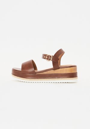 Brown leather platform sandals with a wide front strap, adjustable ankle strap, and a wooden base. Textured white rubber sole.