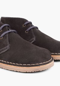 Botas de tobillo de ante negro con punta redonda, costuras en contraste y cordones de textil. Suela duradera en tono marrón claro con agarre texturizado.