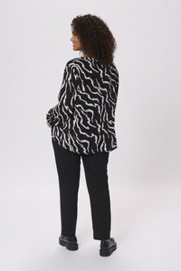 Blouse à rayures zèbres en noir et blanc avec des manches longues, associée à un pantalon noir et des chaussures noires robustes, vue de dos.