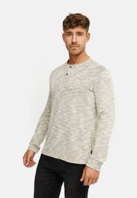 Maglia henley a maniche lunghe di colore grigio chiaro con motivo a trama, caratterizzata da due bottoni al collo e polsini a costine. Abbinata a jeans scuri.