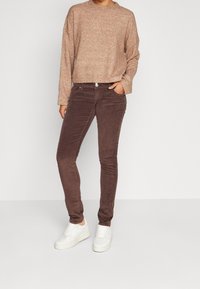 Hnědé kordové kalhoty se slim fit, doplněné o texturovaný béžový svetr. Bílé tenisky s robustní podrážkou dotvářejí celkový outfit.