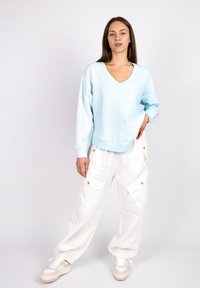 Light blue sweatshirt with a V-neck, oversized fit, and long sleeves. Paired with loose-fitting white cargo pants featuring side pockets and gold buttons.