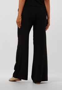 Pantaloni neri a gamba larga realizzati in tessuto morbido, caratterizzati da una texture liscia e da una vestibilità comoda. Abbinati a un paio di scarpe di colore chiaro.