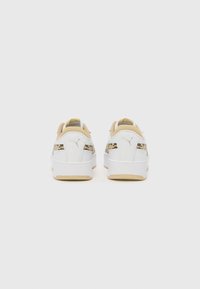 Baskets blanches avec un panneau latéral à motifs beige et noir, en cuir lisse, forme arrondie et semelle extérieure en caoutchouc.