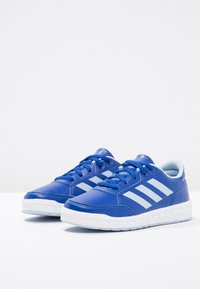 Blå sportskor med en slät syntetisk ovandel, vita tre ränder och en texturerad panel. Har en vit gummisula och blå snören.