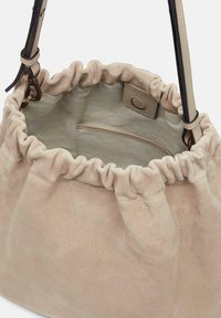 Sac seau en suède rose doux avec un haut froncé, une bandoulière en cuir et une poche intérieure. Texture lisse et design simple avec une esthétique minimaliste.