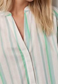 Blusa leggera con righe verticali in bianco, verde chiaro e teal. Presenta un collo senza fascia e una vestibilità comoda.