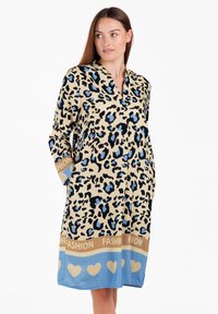 Bata de leopardo en color beige, con manchas azules. Mangas largas con cuello, bolsillos laterales y una banda decorativa con corazones en azul y marrón.