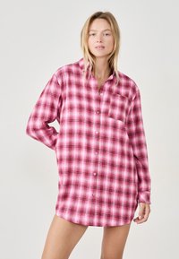 Różowa koszula w kratę z długim rękawem, w odcieniach bieli i ciemniejszych tonach, z zapięciem na guziki z przodu i jedną kieszenią na piersi. Miękka tekstura tkaniny.