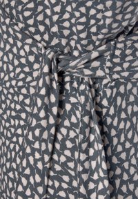 Blau-weißer Stoff mit Mustern und einer Schleifendetails an der Taille, der ein strukturiertes Design aus kleinen Formen sowie ein weiches, dehnbares Material aufweist.