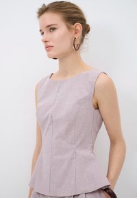Top senza maniche rosa chiaro con design a peplum, caratterizzato da un tessuto testurizzato, scollo rotondo e dettagli di cucitura sottili.