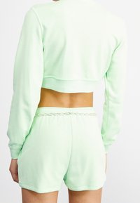 Bakifrån vy av en person som bär en ljusgrön kortärmad sweatshirt och matchande shorts med ett silverkedjebälte i midjan.