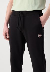 Pantaloni jogger neri con cintura a coste, cordino e tasche laterali. Presentano un logo circolare 'COLMAR' sulla coscia sinistra.