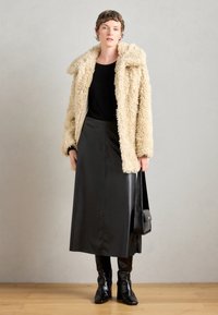 Faux fur beige frakke, sort top, lang sort lædernederdel og knæhøje sorte støvler. Inkluderer en lille sort håndtaske.