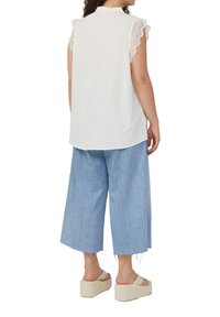 Top sans manches blanc avec des détails en dentelle sur les épaules, associé à un jean coupe courte bleu clair et des sandales à plateforme beiges. Design simple et décontracté.