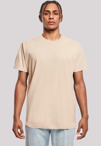 Beige cotton t-shirt with a crew neckline, short sleeves, and a relaxed fit, paired with light blue jeans. Smooth texture, minimal design.