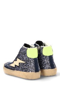 Zapatillas de deporte brillantes en color marino con toques verdes, superficie texturizada, diseño de caña alta, con un rayo beige y una suela gruesa beige.