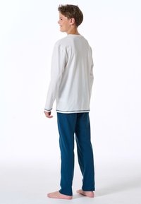White long-sleeve shirt with a rounded neckline, paired with blue pajama pants. Soft fabric, straight cut, minimal stitching accents.