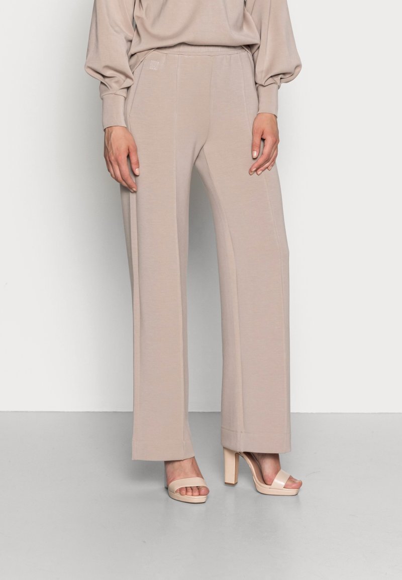 Beiga vida byxor gjorda av mjukt tyg med elastisk midja och sidofickor, ihop med ljusa klacksandaler.