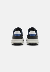 Scarpe sportive con tomaia in suede blu navy, dettagli neri, supporto per il tallone bianco e suola grigia texturizzata con modelli di grip.
