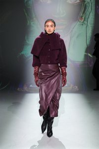 Burgundska volnena pulover z velikim ovratnikom in gumbi, v kombinaciji z slivasto kožno krilo in rdečimi usnjenimi rokavicami. Črne škornje do kolen.