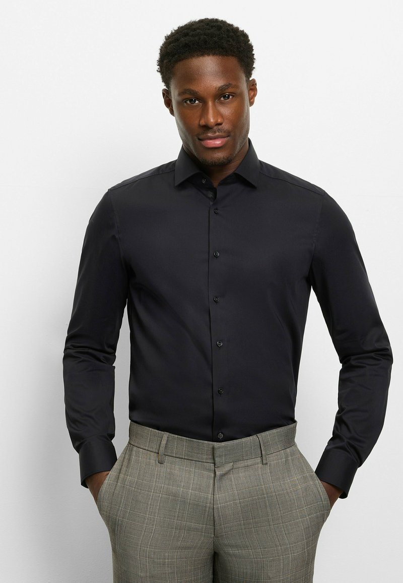 Schwarzes, langärmliges Hemd mit Knöpfen aus glattem Stoff, ausgestattet mit einem spitzen Kragen und schwarzen Knöpfen, kombiniert mit grauen karierten Hosen.