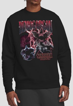 Person wearing black sweatshirt with red and white graphic of Demogorgon monster and lightning, with "Demogorgon" and "Stranger Things" text.