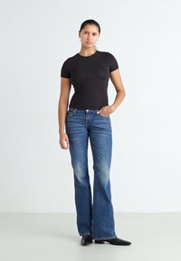 Sort tætsiddende t-shirt og flagrende blå jeans. Jeansene har en falmet tekstur, med et klassisk fem-lommekoncept og subtile syninger.