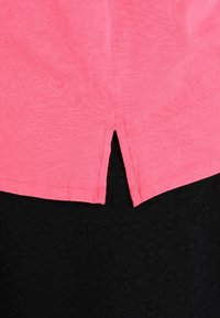 Lyserød T-shirt med rundet kant og en lille slidse bagpå. Fremstillet af blødt stof, den er parret med en tekstureret sort underdel.