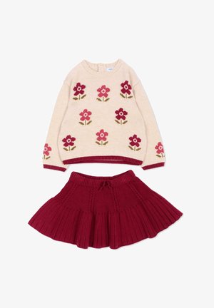 Crèmekleurige trui met rode en roze bloemenpatronen gecombineerd met een rode gebreide geplisseerde rok.