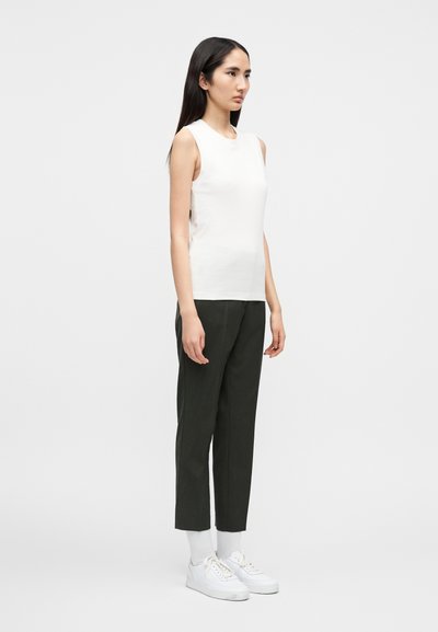 Ελαφρύ λευκό αμάνικο τοπ με στρογγυλεμένο λαιμόκοψη, συνδυασμένο με σκούρο πράσινο παντελόνι με στενή εφαρμογή και λευκά αθλητικά παπούτσια. Ομοιόμορφη υφή σε όλο το ρούχο.