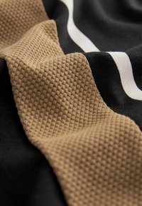 Tissu marron texturé avec un motif nid d'abeille, contrastant avec des rayures lisses noires et blanches, créant une composition multi-texturée.