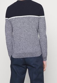 Pull tricot marine et gris avec texture côtelée, présentant une bande blanche horizontale au niveau des épaules et des manches longues.