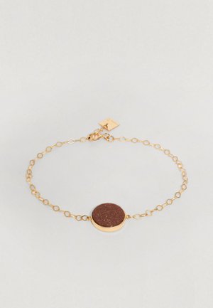 Brățară din lanț de aur cu un centru rotund dintr-o piatră strălucitoare de culoare maro. Lungimile lanțului au textură, iar lângă închizătoare se află o etichetă mică.