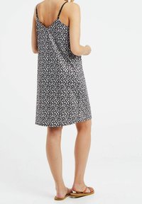 Vestido negro con flores, con tirantes finos, que presenta un corte holgado y un escote en forma de V en la parte posterior. El patrón incluye pequeñas flores blancas y rosas.