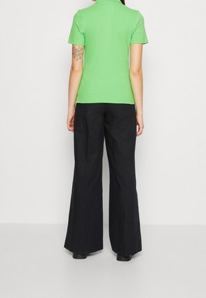 Zielona koszulka polo z krótkim rękawem w połączeniu z czarnymi spodniami o szerokich nogawkach. Górna część ma kołnierzyk, podczas gdy spodnie mają gładką teksturę.