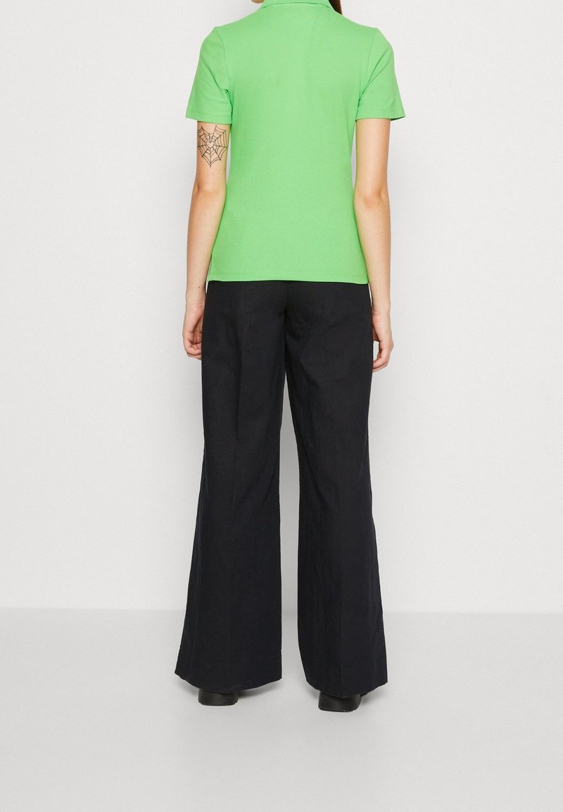 Zielona koszulka polo z krótkim rękawem w połączeniu z czarnymi spodniami o szerokich nogawkach. Górna część ma kołnierzyk, podczas gdy spodnie mają gładką teksturę.